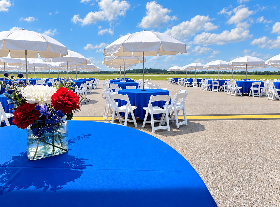 Patriot Club Patriot Club tables with blue linens, white chairs, umbrellas, and floral centerpieces overlooking the flightline.