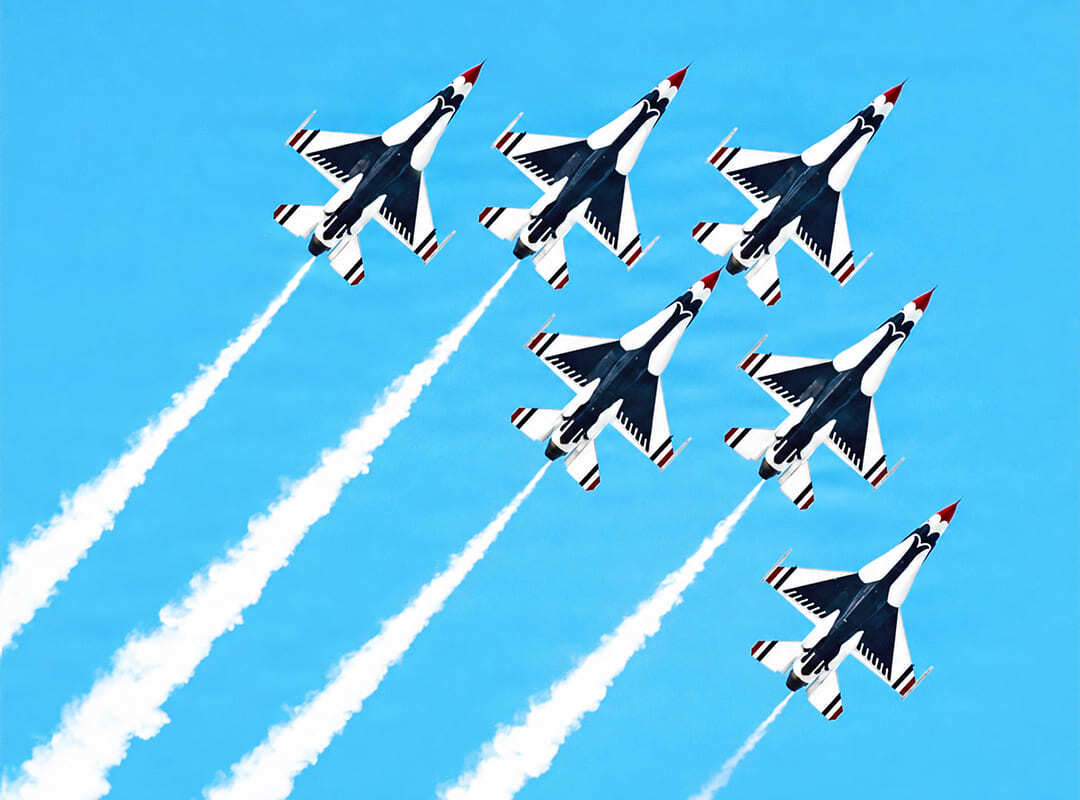Six U.S. Air Force Thunderbirds F-16 Fighting Falcons climb in formation, trailing white smoke against a bright blue sky.