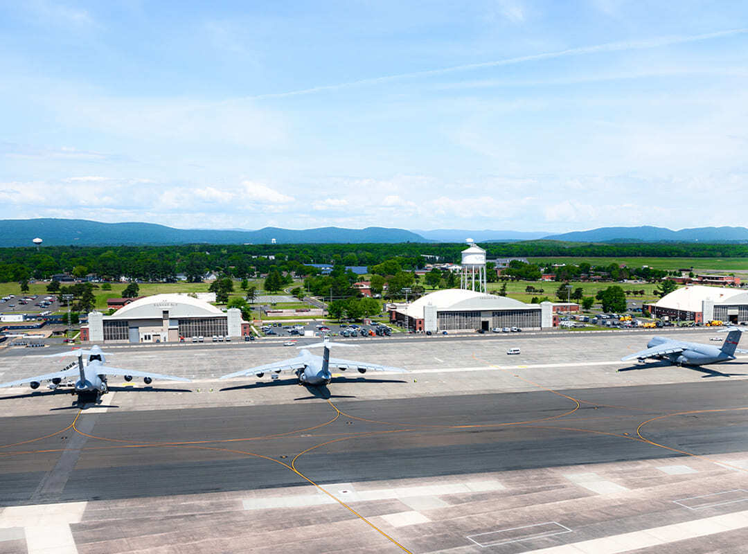 Westover Air Reserve Base Military aircraft parked on the flight line at Westover Air Reserve Base, with hangars, a water tower, and mountains in the distance.